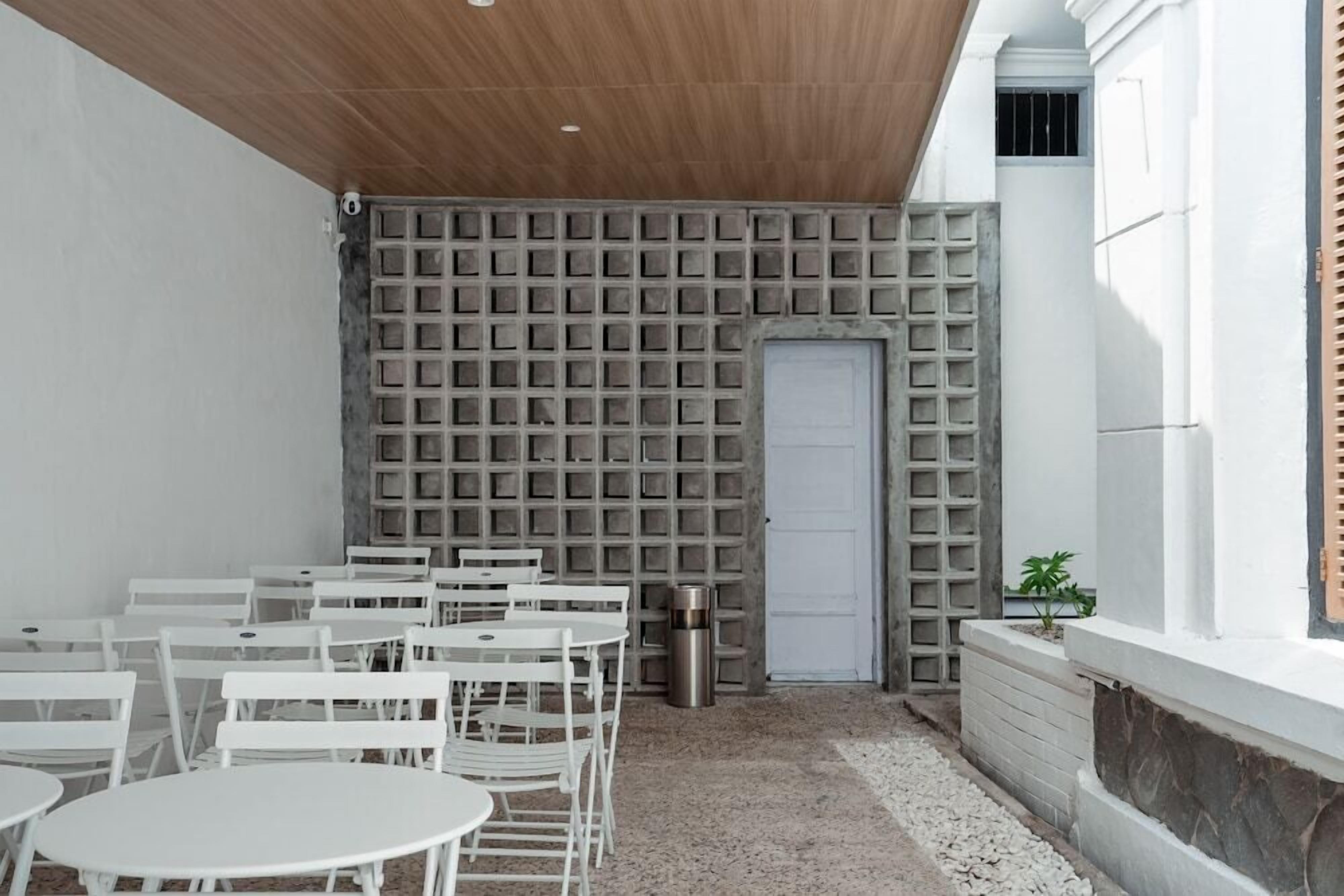 A room with white tables and chairs, a patterned wall, a door, and a small plant.