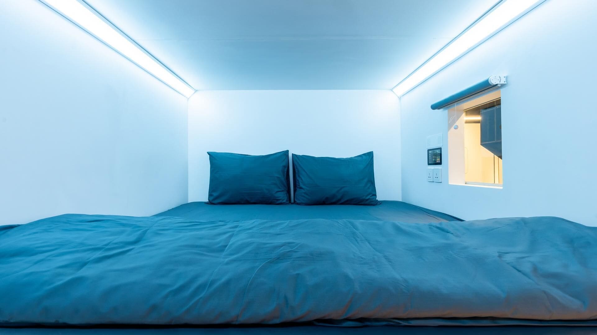 A small, modern bedroom with a bed, two pillows, and a window with a view.