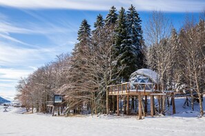 A snow-covered landscape with a glass dome structure, wooden deck, and a small building. - Comfortable panoramic dome in the heart of Vercors (Autrans-Méaudre-en-Vercors)