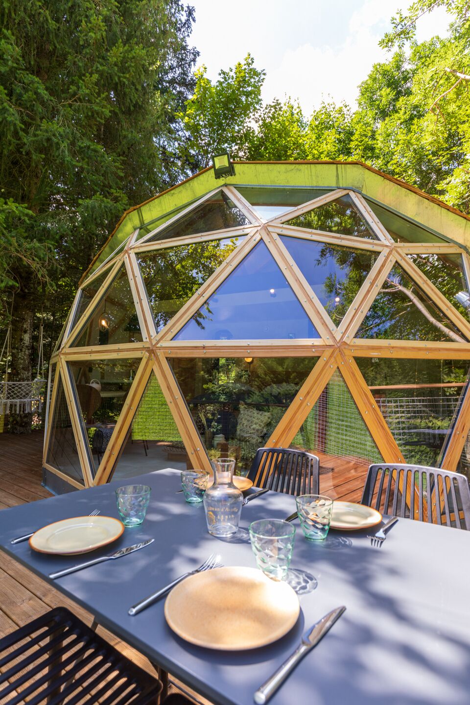 A geodesic dome structure with a table set for dining, surrounded by greenery.