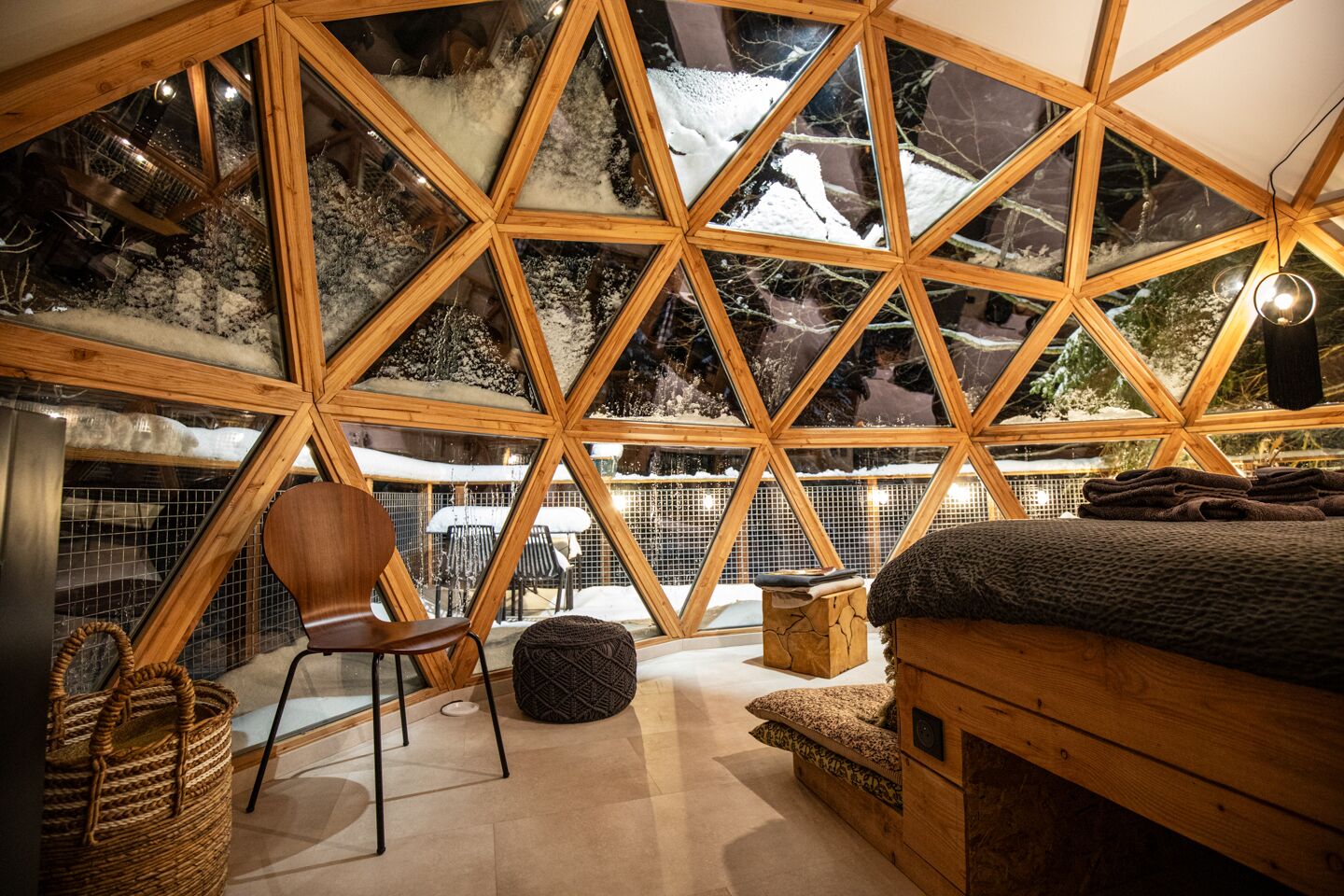 Un intérieur chaleureux au design géométrique, comprenant un lit, un coin salon et offrant une vue sur un paysage enneigé grâce à de grandes fenêtres.