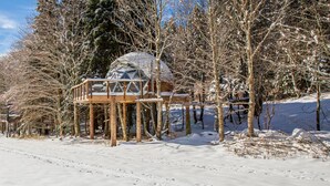 A snow-covered landscape with a wooden cabin structure featuring a dome and a wooden deck. - Comfortable panoramic dome in the heart of Vercors (Autrans-Méaudre-en-Vercors)
