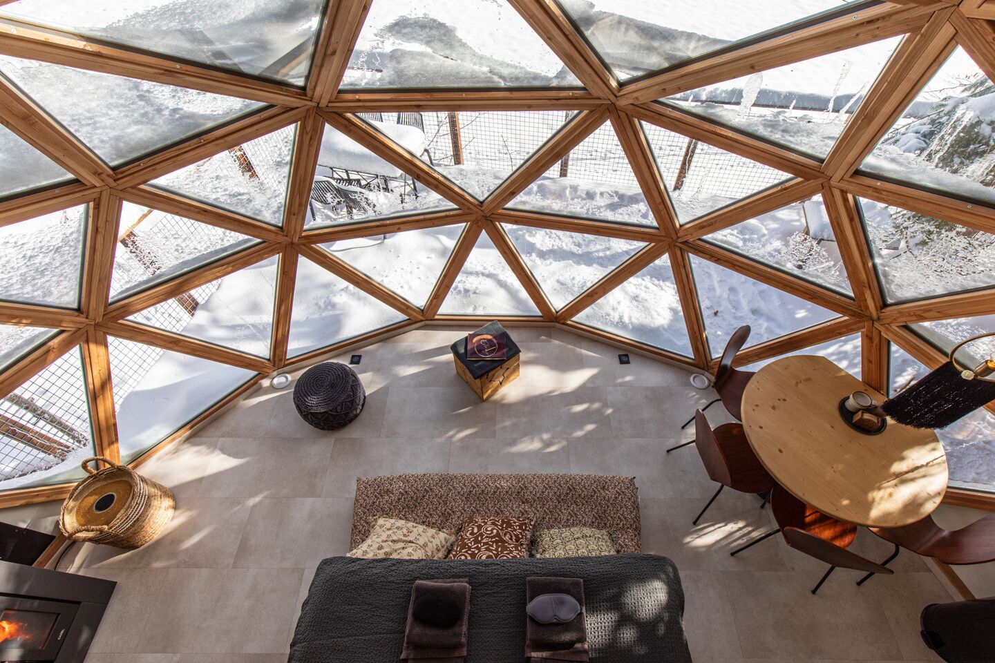 Il s'agit d'une structure en forme de dôme géodésique offrant une vue sur des montagnes enneigées. À l'intérieur, on trouve un espace salon avec une table ronde et des chaises.