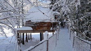 A snow-covered wooden bridge with a metal railing, leading to a building with a snow-covered roof.