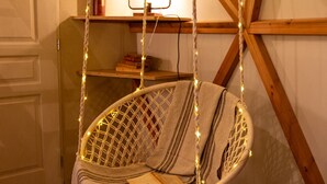 Een gezellige kamer met een hangstoel, houten balken, een plank met boeken en een lamp.