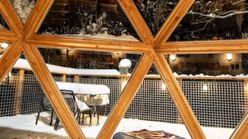 Un espace extérieur enneigé, avec un banc en bois et un livre, vu à travers une structure géométrique en bois.
