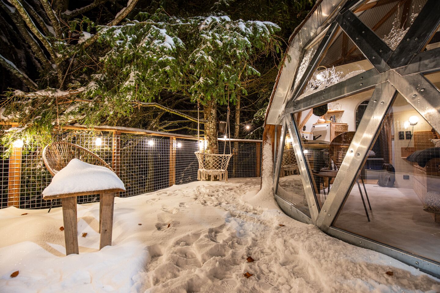 A snow-covered outdoor area with a wooden bench, a swing, and a metal structure.
