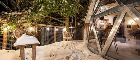 Un espace extérieur enneigé avec un banc en bois, une balançoire et une structure métallique.