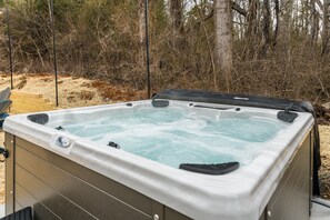 Un jacuzzi en un entorno exterior con una terraza de madera y árboles al fondo.