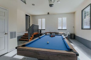 Une table de billard dans une pièce avec un escalier, une porte et une fenêtre.