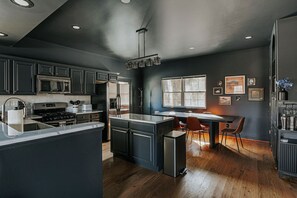 Una cocina moderna con armarios oscuros, una isla central y un comedor con sillas.