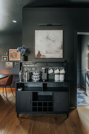 Une cuisine moderne avec un plan de travail noir, un coin café et, au-dessus, un tableau représentant un paysage encadré.