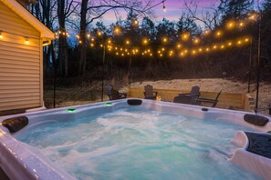 A hot tub with a wooden deck, surrounded by trees and string lights.