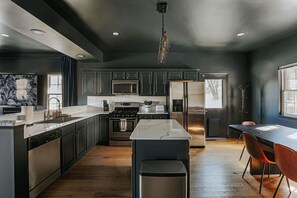 Une cuisine moderne avec des meubles de couleur sombre, des appareils en acier inoxydable et un dosseret en marbre.