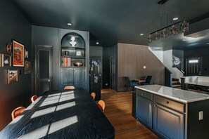 A modern kitchen with dark cabinetry, a central island, and a dining area with a long table and chairs.