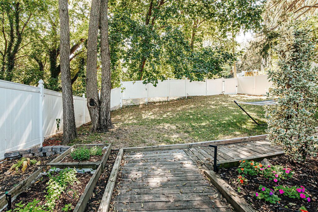 A backyard with raised garden beds, a wooden deck, and a white fence.