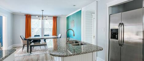 A modern kitchen with a stainless steel refrigerator, granite countertops, and a dining area with a table and chairs.