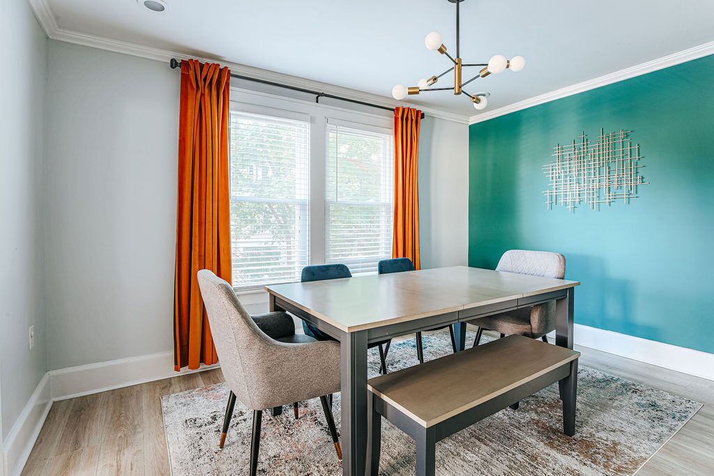 Un espace repas comprenant une table et des chaises, un banc, un luminaire au plafond et un mur orné d’un motif géométrique.