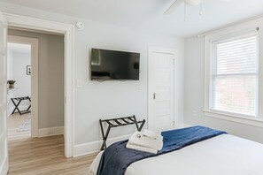 A bedroom with a bed, a TV mounted on the wall, a window with blinds, and a door. - Cozy Craftsman: Newly Renovated/Downtown Staunton (Staunton)