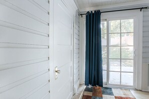 Una puerta blanca con picaporte de latón, cortina azul oscuro y una alfombra estampada sobre piso de madera.