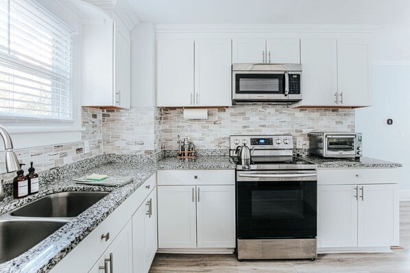 A modern kitchen with white cabinets, a granite countertop, a built-in microwave, a toaster, and a stainless steel oven.