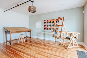 Une pièce comprenant une table en bois, un tabouret, un chevalet avec un tableau, et un luminaire suspendu.