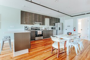 Une cuisine moderne dotée d’appareils électroménagers en acier inoxydable, un coin repas avec des chaises blanches et un plancher en bois.