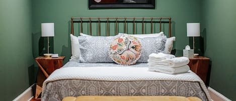 A neatly arranged bedroom with a bed, two bedside tables, a bench, and a framed floral artwork on the wall.