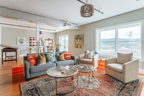 A modern living room with a grey sofa, two round coffee tables, and a large window offering a view of the city.