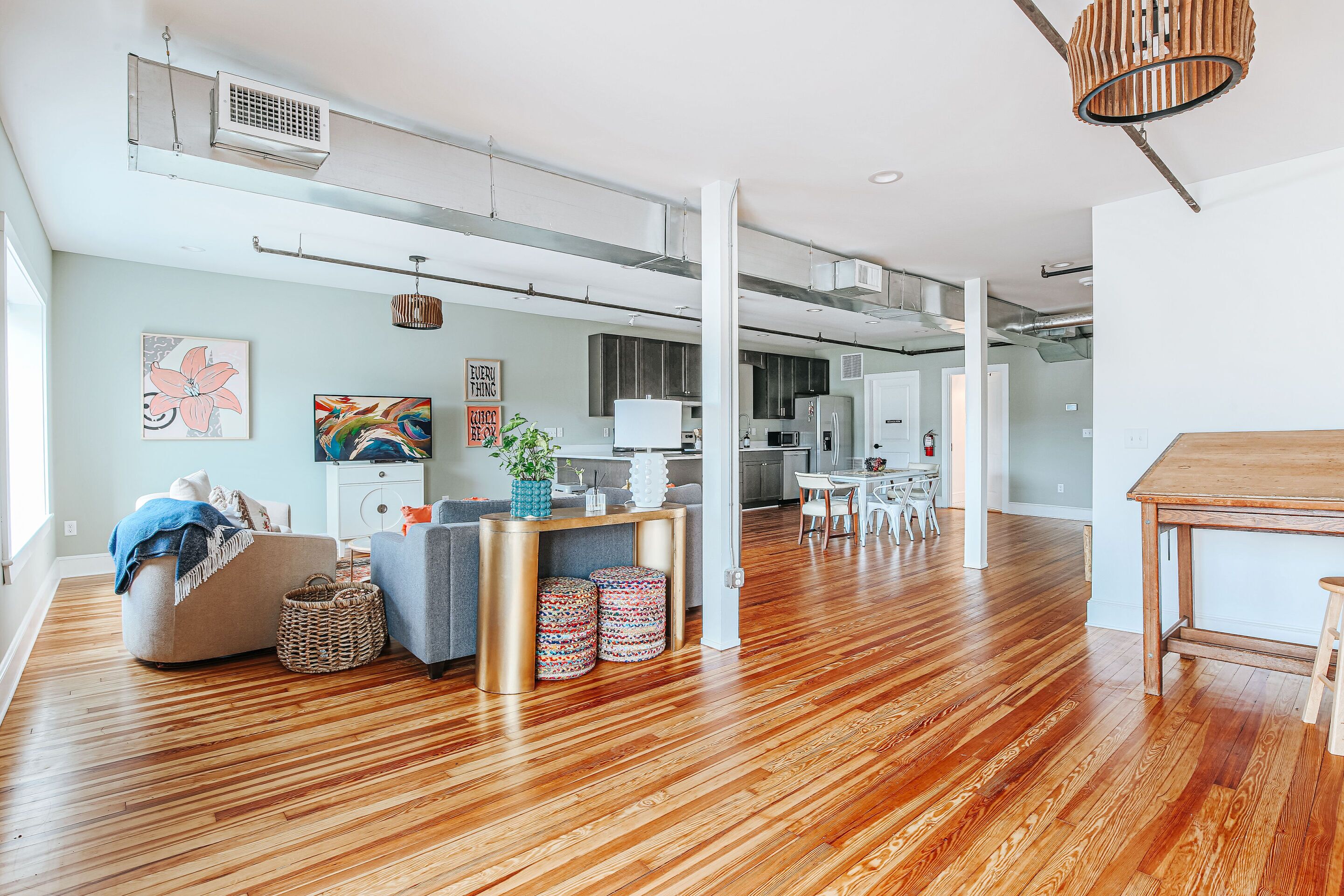 A spacious living area with a wooden floor, a sofa, a dining table, and a kitchen in the background.