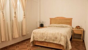 Un dormitorio con una cama de madera, una mesita de noche con una planta y una pequeña mesa con adornos.