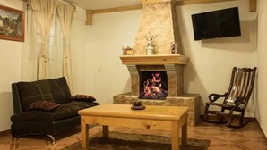 Una sala de estar con chimenea de piedra, un sofá, una mesa de centro de madera y un televisor montado en la pared.