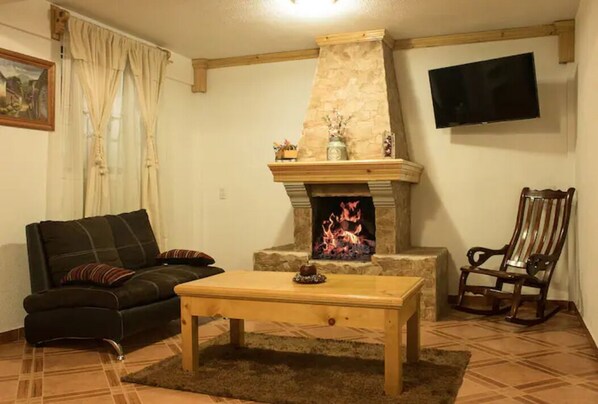 Una sala de estar con chimenea de piedra, un sofá, una mesa de centro de madera y un televisor montado en la pared.