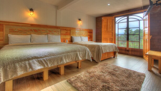 Un dormitorio con dos camas, cabecero de madera, un ventanal con vistas y una mesita.