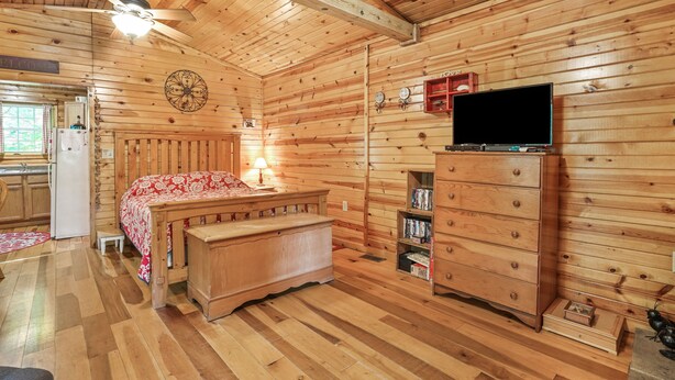 A wooden cabin room with a bed, a dresser, a television, and a ceiling fan. - Whip-poor-will Cabin | Hocking Hills, Firepit (Rockbridge)