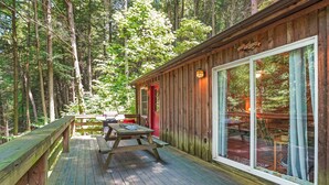 A wooden cabin with a deck, a picnic table, and a large window. - Whip-poor-will Cabin | Hocking Hills, Firepit (Rockbridge)
