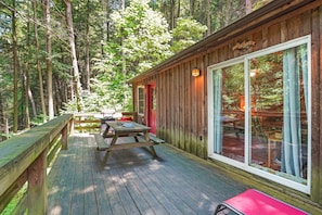 A wooden cabin with a deck, large windows, and a picnic table.