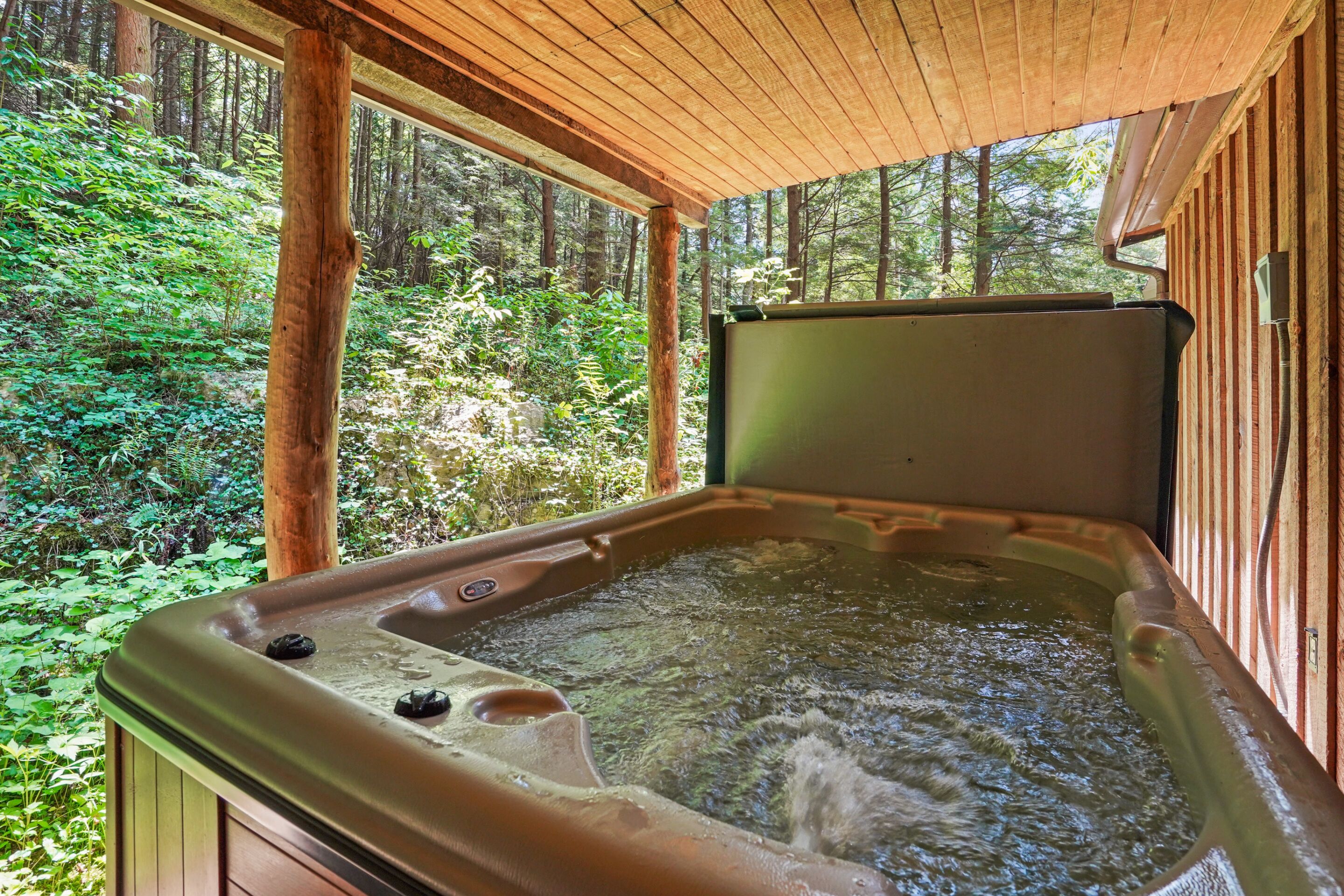 A hot tub with a wooden deck and a forest view.
