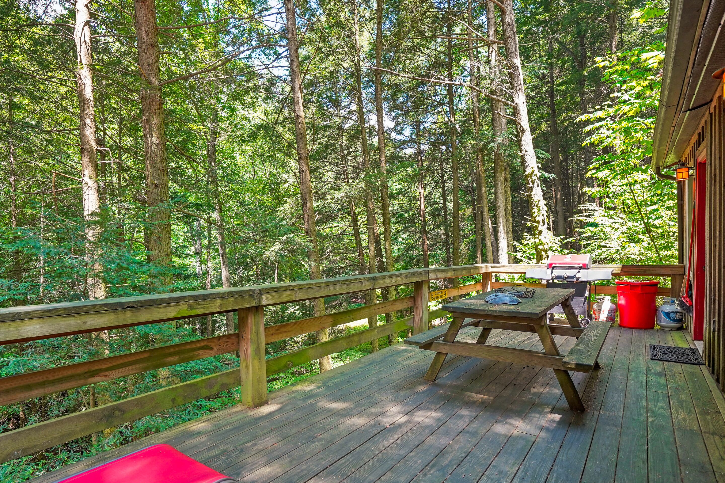 A wooden deck with picnic tables and a barbecue grill, surrounded by a forest.