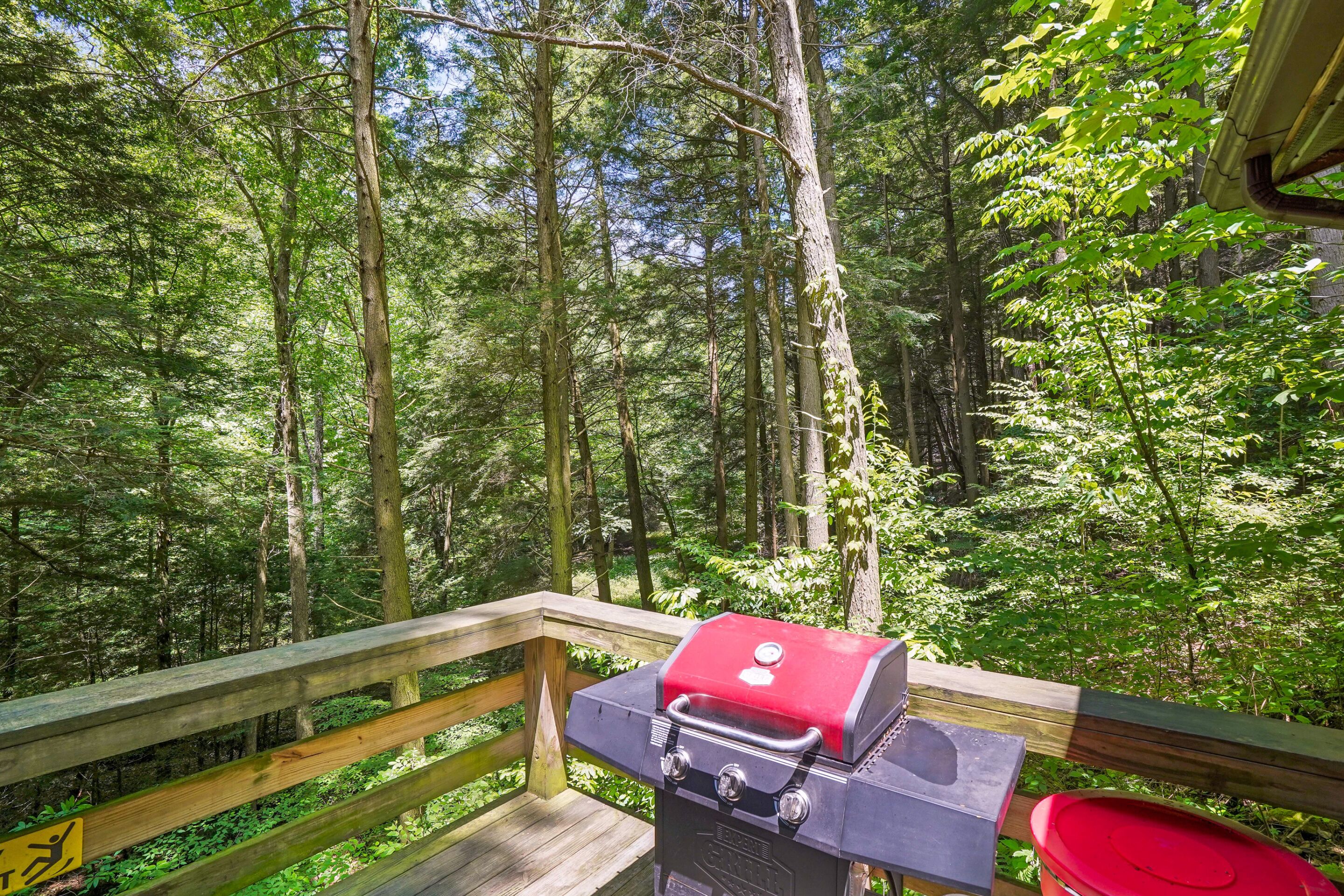 A deck with a barbecue grill overlooking a forested area.