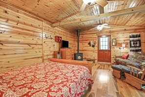 Ein Holzblockhaus-Interieur mit Bett, Sofa, Kamin und Fernseher.