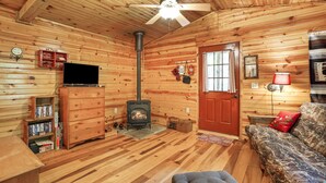 A cozy cabin interior with a fireplace, wooden walls, a ceiling fan, a television, and a couch. - Whip-poor-will Cabin | Hocking Hills, Firepit (Rockbridge)
