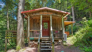 A wooden cabin with a red door, a porch, and a small staircase leading up to the entrance. - Whip-poor-will Cabin | Hocking Hills, Firepit (Rockbridge)