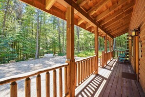 A wooden cabin with a covered porch overlooking a forest.
