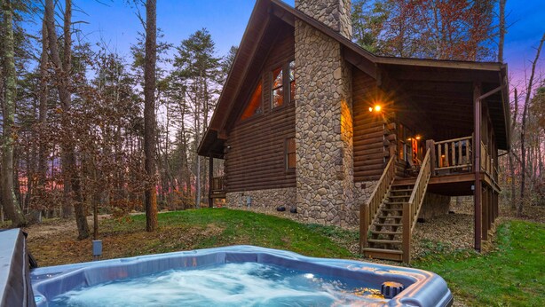 Een blokhut met een stenen gevel, een hottub en een houten terras.