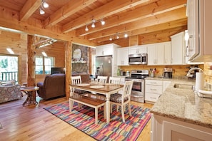 A wooden cabin interior with a dining area, kitchen, and living room.