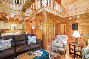 A wooden cabin interior with a living area featuring a brown leather sofa, patterned armchairs, and a small round table with a lamp.