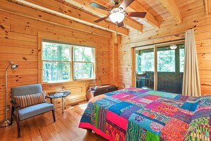 A wooden cabin room with a large bed, a chair, a table, and a ceiling fan.