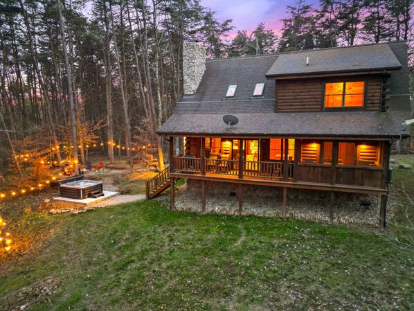 A log cabin with a deck, a hot tub, and string lights.