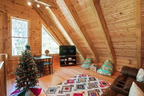 Una camera mansardata accogliente con soffitto in legno, televisore, albero di Natale e tappeto decorato.
